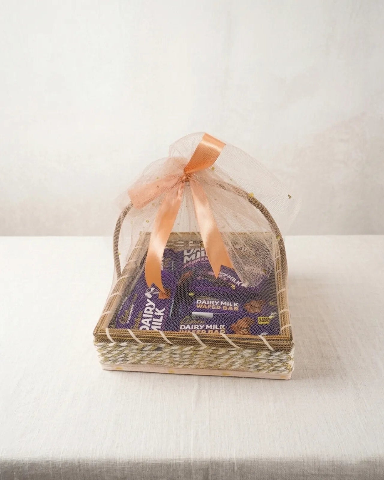 Woven 10x10 basket with Cadbury Dairy Milk Wafer Bars, Dairy Milk bars and Dairy Milk Bubbly wrapped in peach organza gift hamper by The Love Language Pakistan